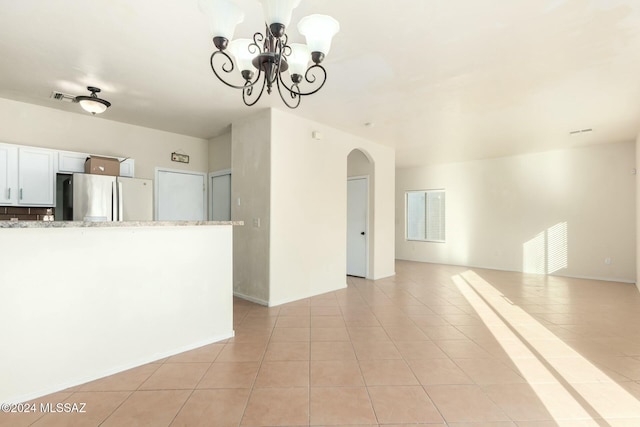 interior space with stainless steel refrigerator, light tile patterned floors, an inviting chandelier, light stone counters, and white cabinets