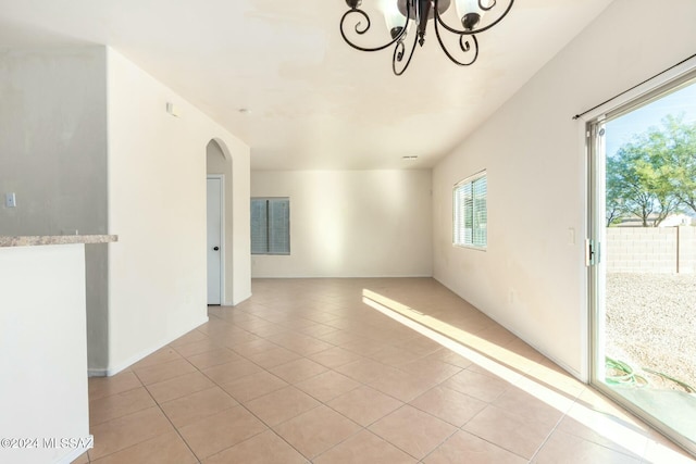 spare room with a chandelier, light tile patterned floors, and plenty of natural light