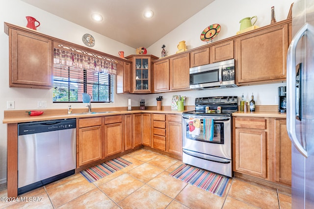 kitchen with sink, light tile patterned floors, vaulted ceiling, and appliances with stainless steel finishes