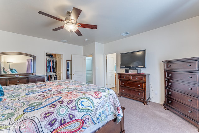 bedroom with ceiling fan, a closet, a spacious closet, and light carpet