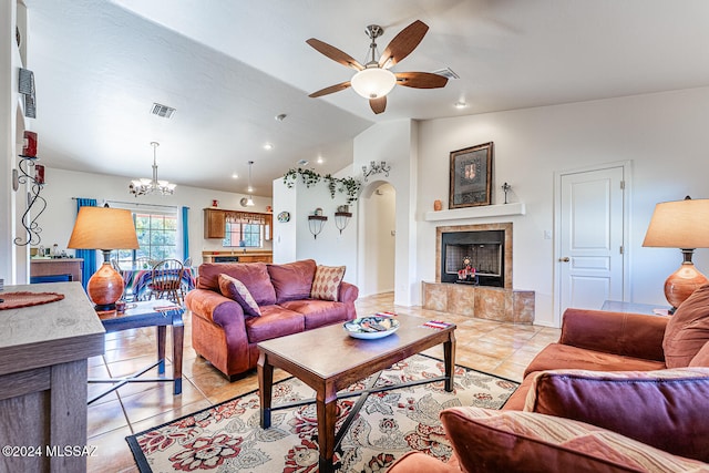 living room featuring vaulted ceiling, a tiled fireplace, light tile patterned floors, and ceiling fan with notable chandelier