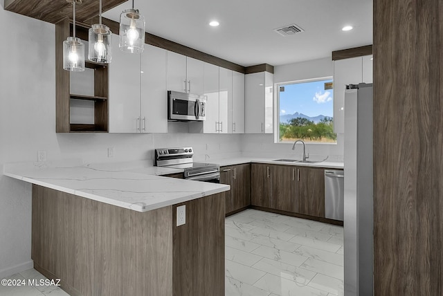 kitchen featuring sink, kitchen peninsula, appliances with stainless steel finishes, decorative light fixtures, and white cabinetry