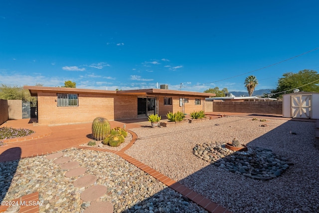 rear view of house featuring a patio, fence private yard, brick siding, an outdoor structure, and a shed