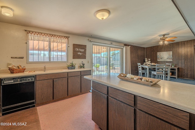 kitchen featuring dishwasher, light countertops, dark brown cabinets, wood walls, and a sink