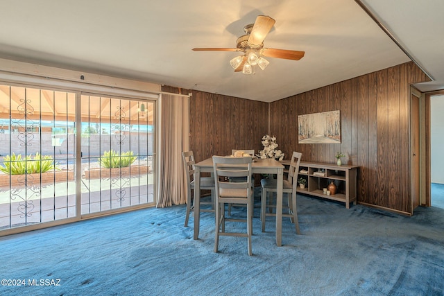 dining room with carpet floors, wood walls, and a ceiling fan