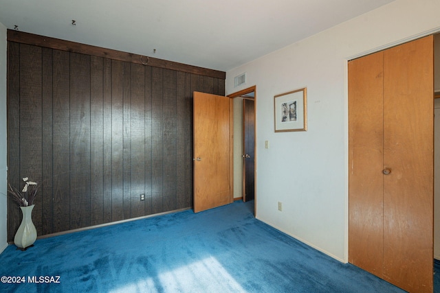 unfurnished bedroom with wood walls, dark carpet, and visible vents