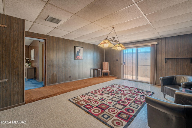 living room with wooden walls, visible vents, a drop ceiling, and carpet flooring