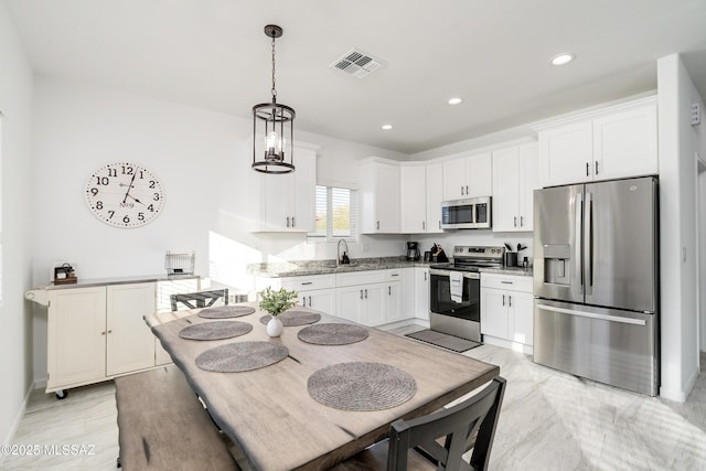 kitchen with a sink, visible vents, white cabinets, hanging light fixtures, and appliances with stainless steel finishes