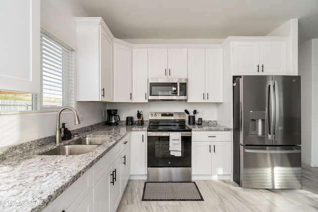 kitchen with light stone counters, appliances with stainless steel finishes, a sink, and white cabinetry