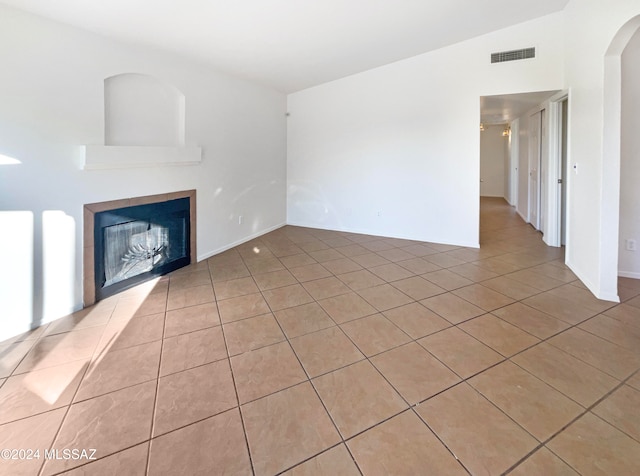 unfurnished living room featuring a tiled fireplace, light tile patterned flooring, and vaulted ceiling