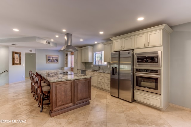 kitchen featuring backsplash, island exhaust hood, a breakfast bar area, stainless steel appliances, and light stone counters