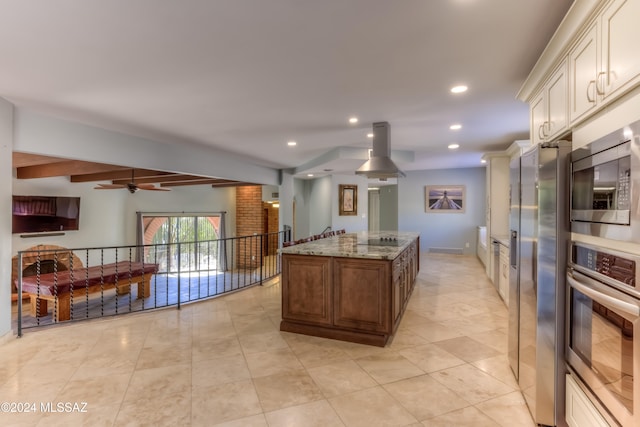 kitchen featuring ceiling fan, stainless steel appliances, beamed ceiling, stone countertops, and a center island