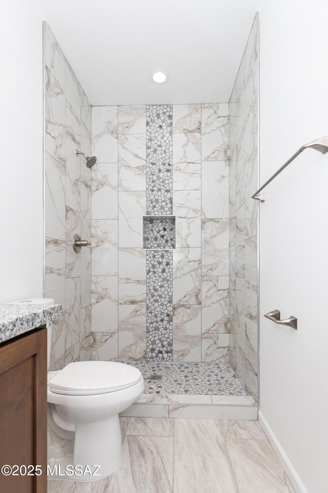 bathroom featuring a tile shower, vanity, and toilet