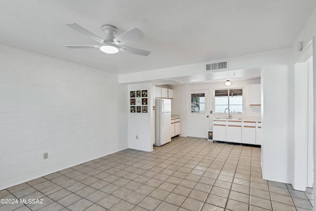 kitchen with white cabinets, sink, ceiling fan, white fridge, and brick wall