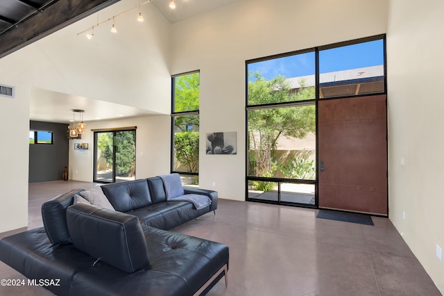 living room with an inviting chandelier, rail lighting, a towering ceiling, concrete floors, and beamed ceiling