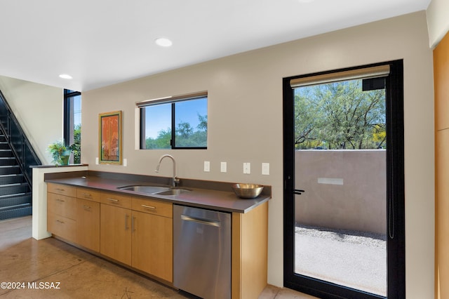 kitchen with dark countertops, recessed lighting, stainless steel dishwasher, a sink, and concrete floors