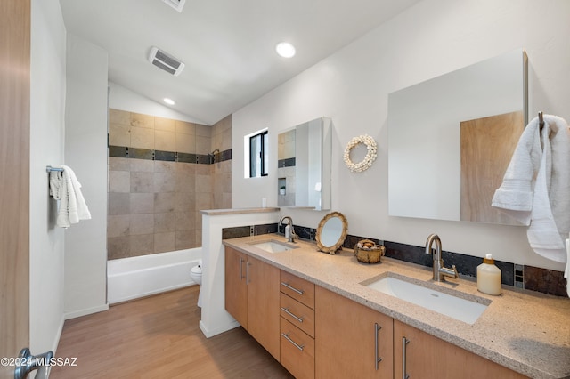 full bathroom featuring tiled shower / bath combo, vanity, hardwood / wood-style flooring, toilet, and lofted ceiling