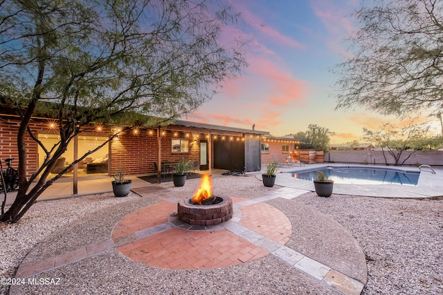 patio terrace at dusk with a fire pit and a fenced in pool