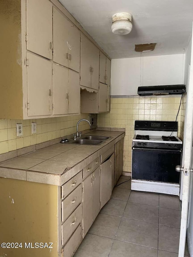 kitchen with decorative backsplash, gas range gas stove, sink, tile counters, and light tile patterned flooring