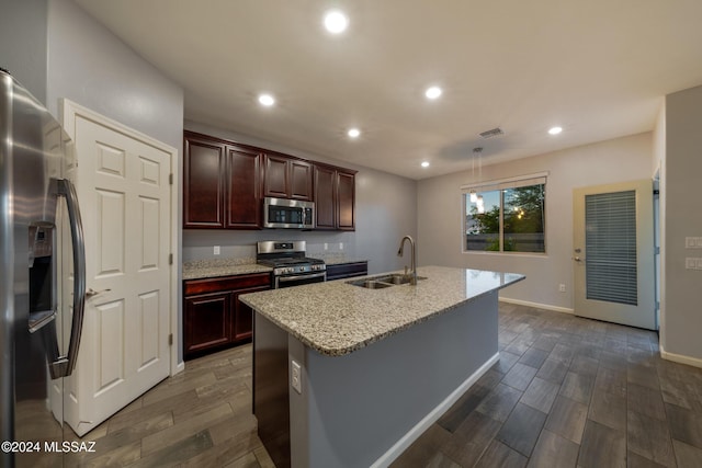 kitchen with dark wood-type flooring, sink, stainless steel appliances, and a center island with sink