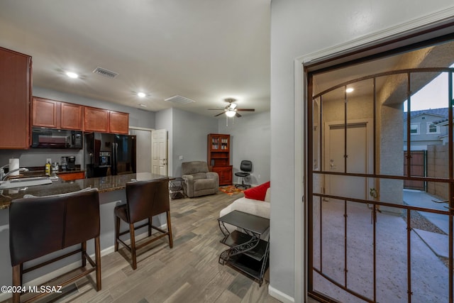 kitchen featuring a kitchen breakfast bar, ceiling fan, sink, black appliances, and light hardwood / wood-style floors