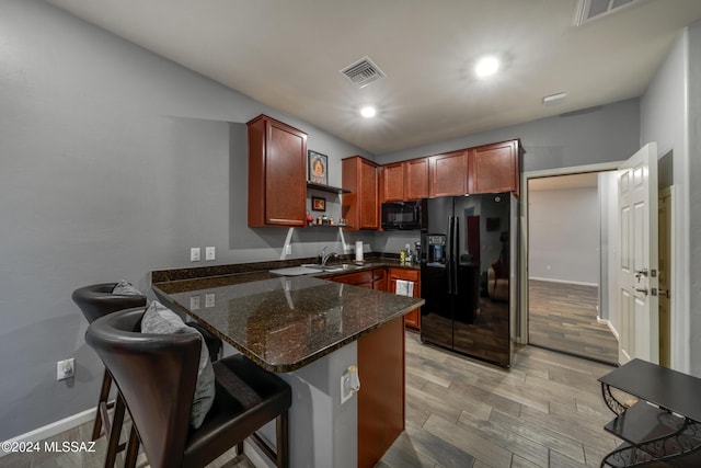 kitchen with kitchen peninsula, a kitchen breakfast bar, black appliances, dark stone countertops, and light hardwood / wood-style floors