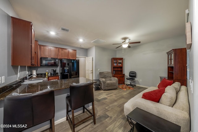 kitchen with black appliances, a kitchen breakfast bar, sink, ceiling fan, and dark hardwood / wood-style flooring