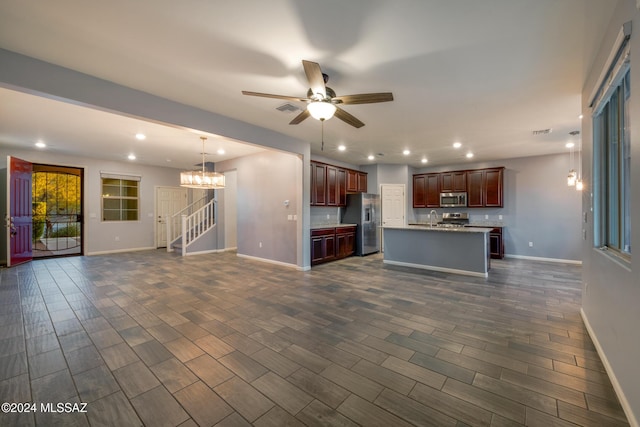 kitchen featuring ceiling fan with notable chandelier, appliances with stainless steel finishes, dark hardwood / wood-style flooring, and an island with sink