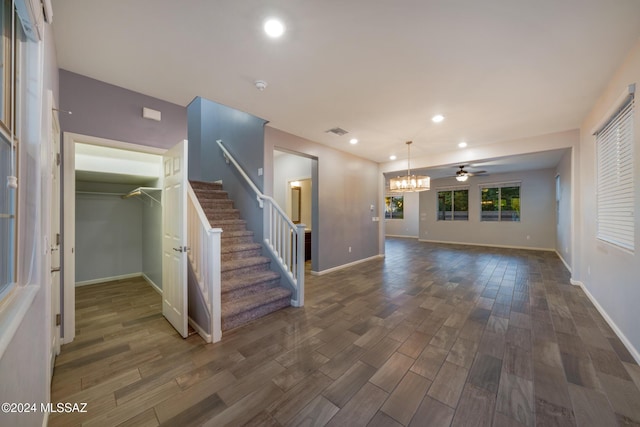 unfurnished living room with ceiling fan with notable chandelier and dark hardwood / wood-style flooring