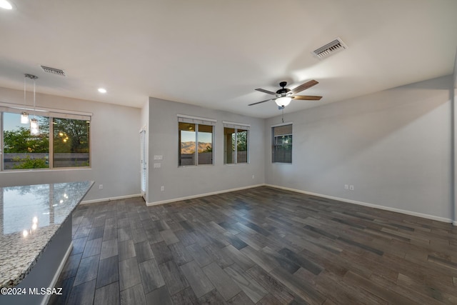 empty room featuring plenty of natural light, ceiling fan, and dark wood-type flooring