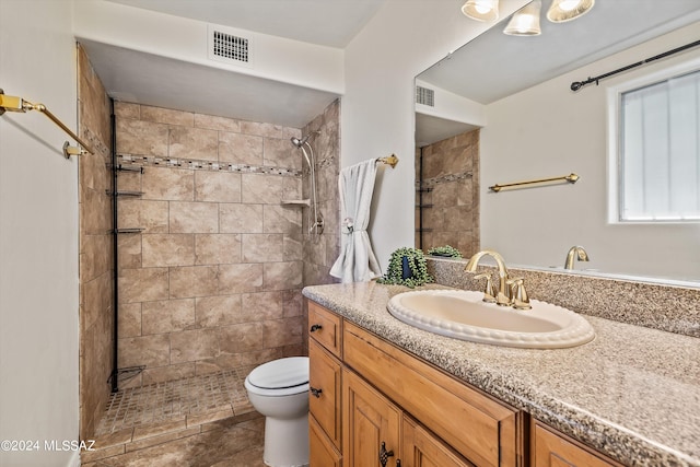 bathroom with tiled shower, tile patterned flooring, vanity, and toilet