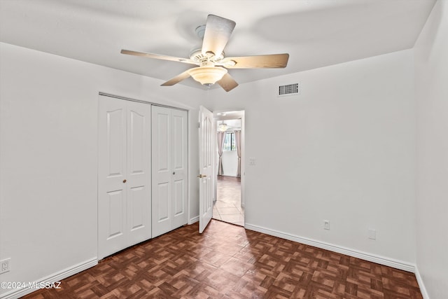 unfurnished bedroom with ceiling fan, a closet, and dark parquet floors