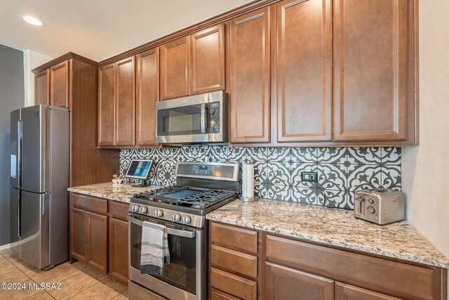 6551 E Via Arroyo Largo, Tucson, AZ 85756 - kitchen with appliances with stainless steel finishes, backsplash, light stone countertops, and brown cabinets