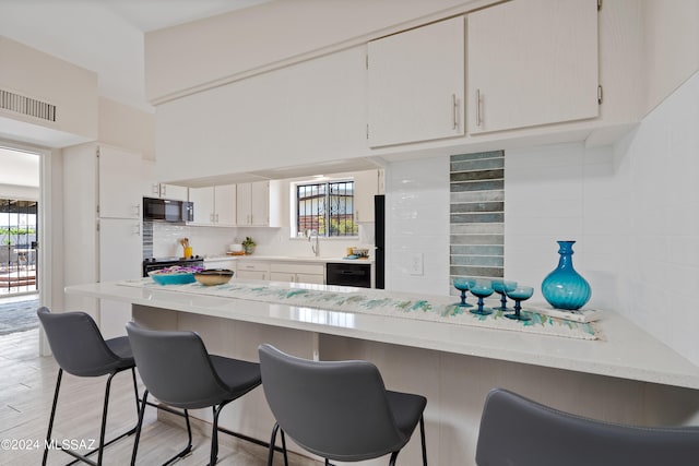 kitchen with decorative backsplash, kitchen peninsula, light wood-type flooring, black appliances, and white cabinetry