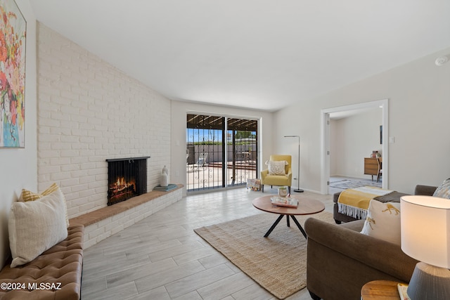 living room featuring vaulted ceiling, light wood-type flooring, and a brick fireplace