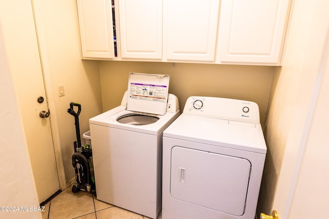 laundry area featuring washing machine and dryer, light tile patterned floors, and cabinets