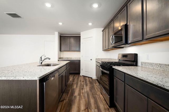 kitchen with a center island with sink, sink, dark brown cabinets, dark hardwood / wood-style flooring, and stainless steel appliances