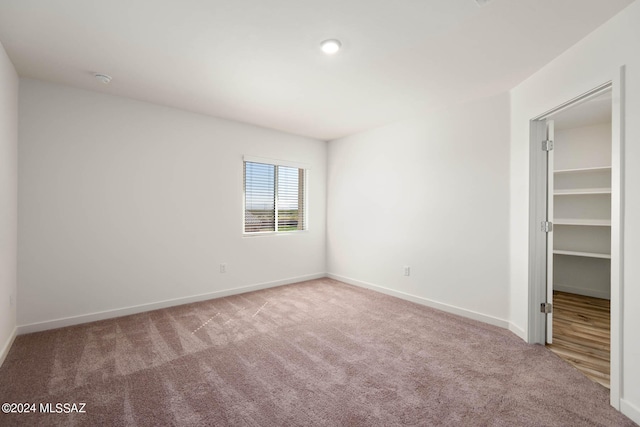 unfurnished bedroom with a walk in closet, a closet, and light colored carpet