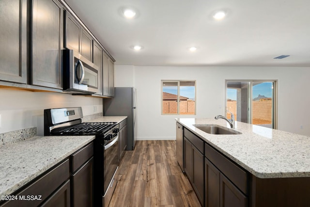 kitchen with a kitchen island with sink, dark wood-type flooring, sink, light stone countertops, and appliances with stainless steel finishes