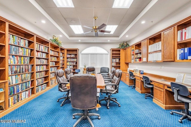 home office featuring a raised ceiling, ceiling fan, carpet, and built in desk