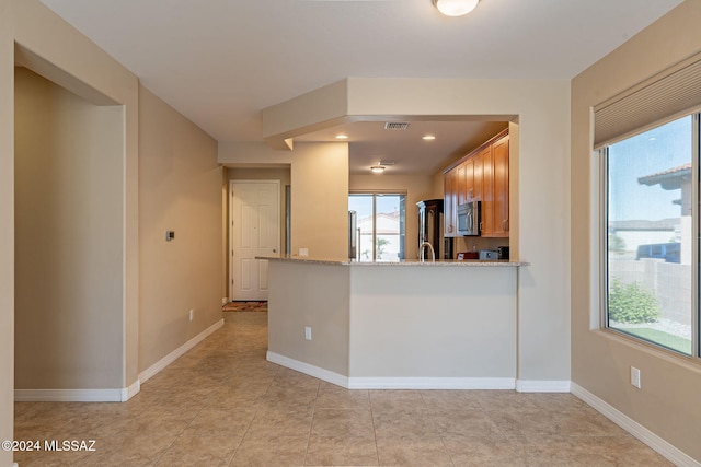 kitchen with stainless steel microwave, visible vents, brown cabinetry, a peninsula, and baseboards