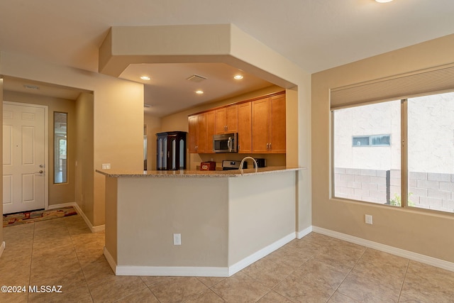 kitchen featuring light stone countertops, baseboards, stainless steel microwave, and brown cabinets