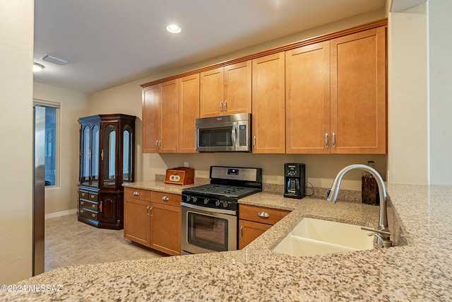 kitchen featuring brown cabinets, stainless steel appliances, visible vents, a sink, and light stone countertops