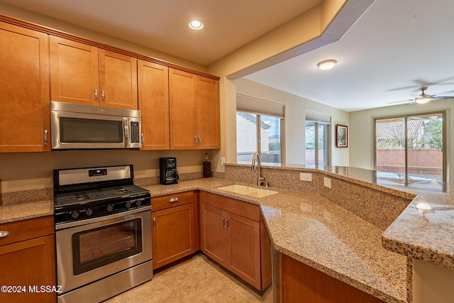 kitchen with light tile patterned flooring, stainless steel appliances, a sink, light stone countertops, and brown cabinetry