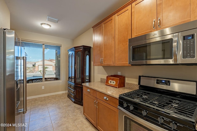 kitchen with light stone counters, light tile patterned flooring, stainless steel appliances, visible vents, and brown cabinetry