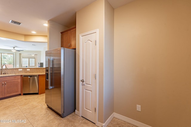 kitchen featuring visible vents, brown cabinetry, light stone countertops, stainless steel appliances, and a sink