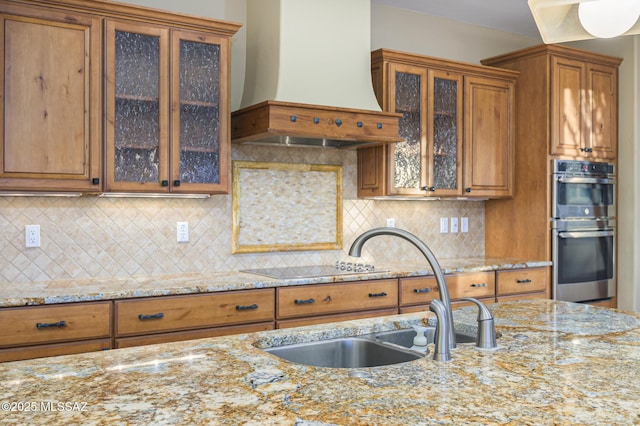 4594 S Moon River Pl, Green Valley, AZ 85622 - kitchen with wall chimney range hood, stainless steel double oven, brown cabinets, and light stone counters