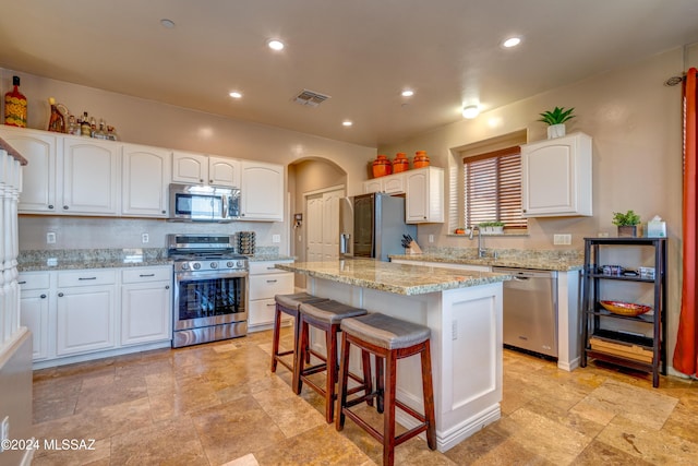 kitchen with arched walkways, appliances with stainless steel finishes, a center island, light stone countertops, and a kitchen bar