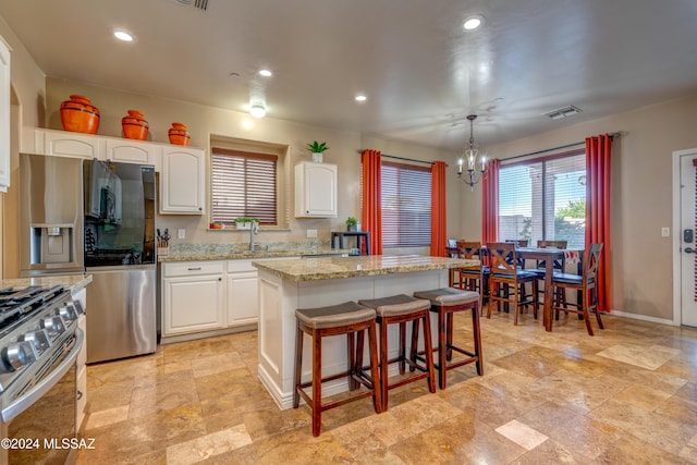 kitchen featuring visible vents, a kitchen island, appliances with stainless steel finishes, light stone counters, and a kitchen bar