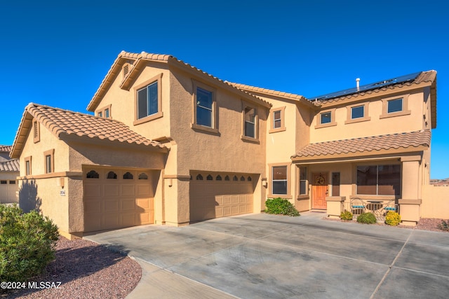 mediterranean / spanish home featuring a tile roof, solar panels, stucco siding, an attached garage, and driveway